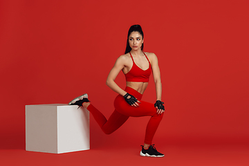 Image showing Beautiful young female athlete practicing on red studio background, monochrome portrait