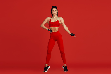 Image showing Beautiful young female athlete practicing on red studio background, monochrome portrait