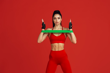 Image showing Beautiful young female athlete practicing on red studio background, monochrome portrait