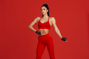 Image showing Beautiful young female athlete practicing on red studio background, monochrome portrait