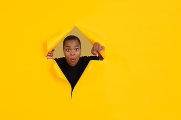 Image showing Cheerful young woman poses in torn yellow paper hole background, emotional and expressive