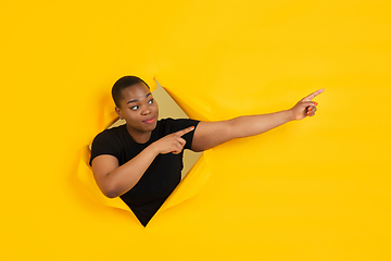 Image showing Cheerful young woman poses in torn yellow paper hole background, emotional and expressive