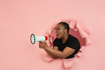 Image showing Cheerful young woman poses in torn coral paper hole background, emotional and expressive, shouting with speaker