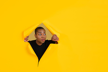 Image showing Cheerful young woman poses in torn yellow paper hole background, emotional and expressive