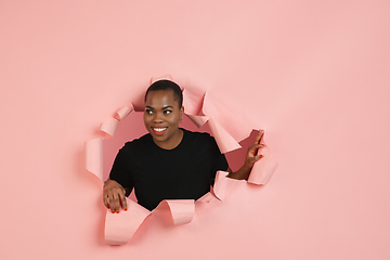 Image showing Cheerful young woman poses in torn coral paper hole background, emotional and expressive