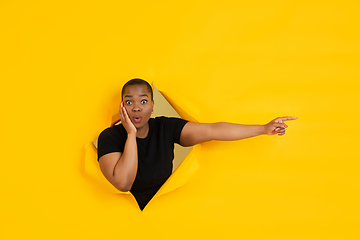 Image showing Cheerful young woman poses in torn yellow paper hole background, emotional and expressive