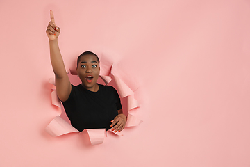 Image showing Cheerful young woman poses in torn coral paper hole background, emotional and expressive