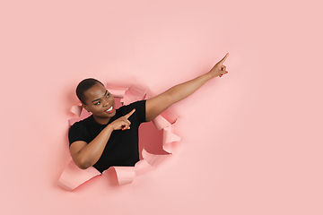 Image showing Cheerful young woman poses in torn coral paper hole background, emotional and expressive