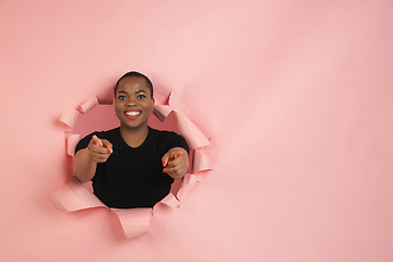Image showing Cheerful young woman poses in torn coral paper hole background, emotional and expressive