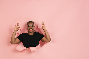 Image showing Cheerful young woman poses in torn coral paper hole background, emotional and expressive