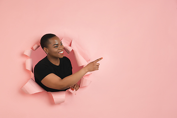 Image showing Cheerful young woman poses in torn coral paper hole background, emotional and expressive