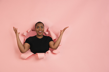 Image showing Cheerful young woman poses in torn coral paper hole background, emotional and expressive