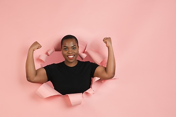 Image showing Cheerful young woman poses in torn coral paper hole background, emotional and expressive