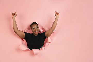 Image showing Cheerful young woman poses in torn coral paper hole background, emotional and expressive