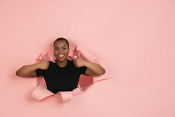 Image showing Cheerful young woman poses in torn coral paper hole background, emotional and expressive