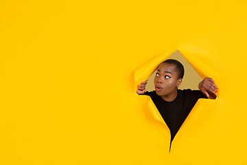 Image showing Cheerful young woman poses in torn yellow paper hole background, emotional and expressive