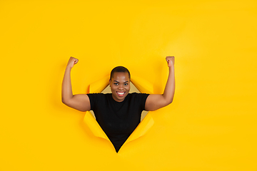 Image showing Cheerful young woman poses in torn yellow paper hole background, emotional and expressive