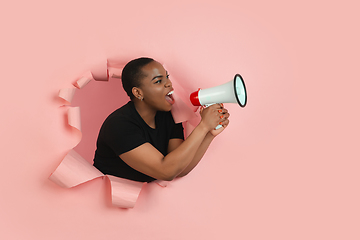 Image showing Cheerful young woman poses in torn coral paper hole background, emotional and expressive, shouting with speaker