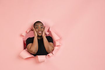 Image showing Cheerful young woman poses in torn coral paper hole background, emotional and expressive