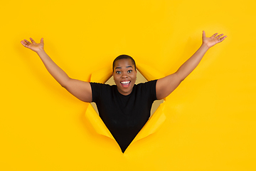 Image showing Cheerful young woman poses in torn yellow paper hole background, emotional and expressive