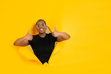 Image showing Cheerful young woman poses in torn yellow paper hole background, emotional and expressive