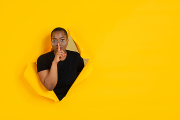 Image showing Cheerful young woman poses in torn yellow paper hole background, emotional and expressive