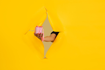 Image showing Female hand giving gift in torn yellow paper hole background, celebration