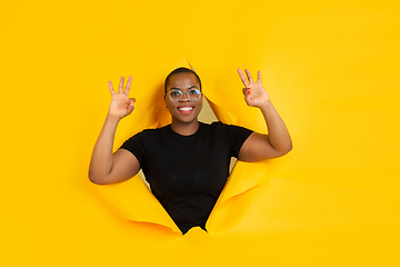 Image showing Cheerful young woman poses in torn yellow paper hole background, emotional and expressive