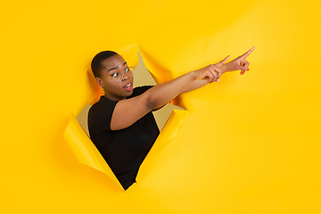 Image showing Cheerful young woman poses in torn yellow paper hole background, emotional and expressive