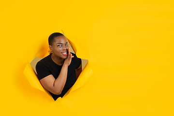 Image showing Cheerful young woman poses in torn yellow paper hole background, emotional and expressive