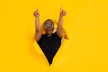 Image showing Cheerful young woman poses in torn yellow paper hole background, emotional and expressive