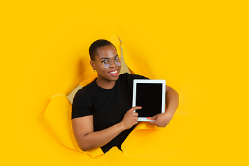 Image showing Cheerful young woman poses in torn yellow paper hole background, emotional and expressive