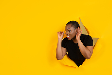 Image showing Cheerful young woman poses in torn yellow paper hole background, emotional and expressive