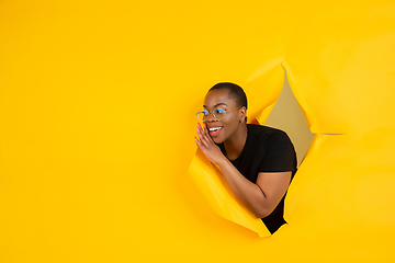 Image showing Cheerful young woman poses in torn yellow paper hole background, emotional and expressive