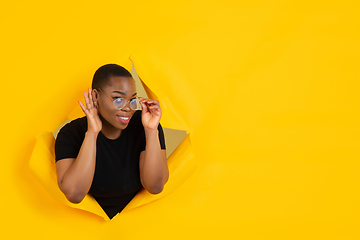 Image showing Cheerful young woman poses in torn yellow paper hole background, emotional and expressive