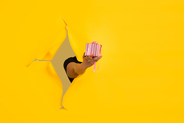 Image showing Female hand giving gift in torn yellow paper hole background, celebration