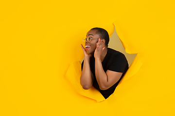 Image showing Cheerful young woman poses in torn yellow paper hole background, emotional and expressive, shouting with speaker