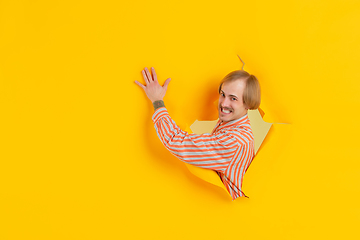 Image showing Cheerful young man poses in torn yellow paper hole background, emotional and expressive