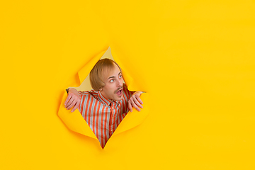 Image showing Cheerful young man poses in torn yellow paper hole background, emotional and expressive