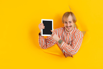 Image showing Cheerful young man poses in torn yellow paper hole background, emotional and expressive