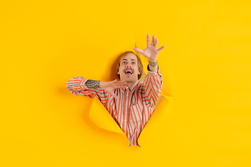 Image showing Cheerful young man poses in torn yellow paper hole background, emotional and expressive