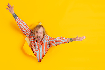 Image showing Cheerful young man poses in torn yellow paper hole background, emotional and expressive