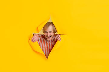 Image showing Cheerful young man poses in torn yellow paper hole background, emotional and expressive