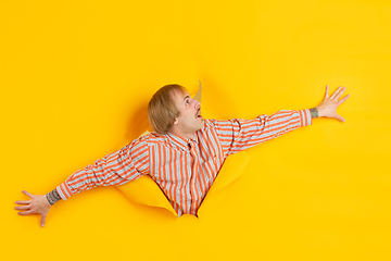 Image showing Cheerful young man poses in torn yellow paper hole background, emotional and expressive