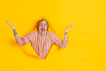 Image showing Cheerful young man poses in torn yellow paper hole background, emotional and expressive