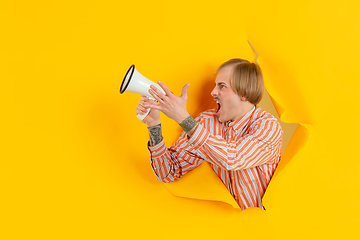 Image showing Cheerful young man poses in torn yellow paper hole background, emotional and expressive