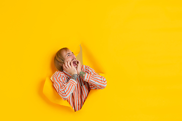 Image showing Cheerful young man poses in torn yellow paper hole background, emotional and expressive