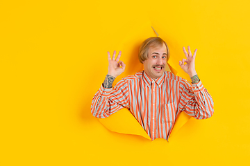 Image showing Cheerful young man poses in torn yellow paper hole background, emotional and expressive