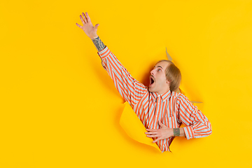 Image showing Cheerful young man poses in torn yellow paper hole background, emotional and expressive