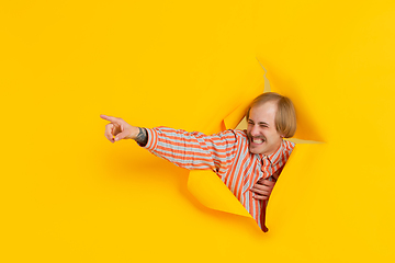 Image showing Cheerful young man poses in torn yellow paper hole background, emotional and expressive